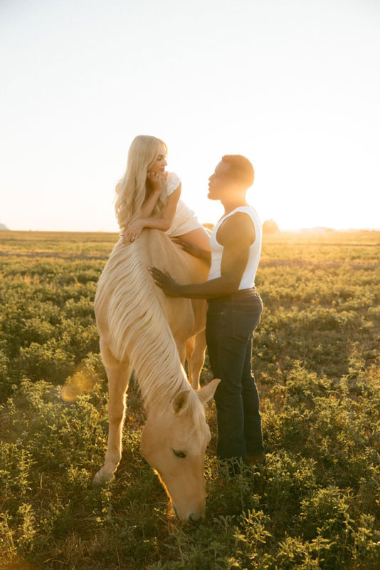Bride with lond blonde Hairalicious wig sitting on a white horse at golden-hour sunset for engagement photos