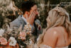 Bride with lace wedding dress with long braided blonde hair as her groom wipes a happy tear, wearing a Hairalicious wig
