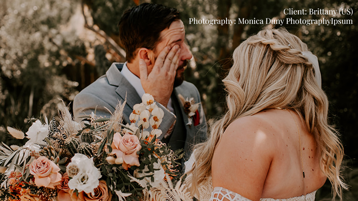 Bride with lace wedding dress with long braided blonde hair as her groom wipes a happy tear, wearing a Hairalicious wig